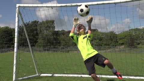 Young Goalkeeper saves the ball in a soccer / football match. The boy dives and catches the ball to prevent a goal. Super Slow motion