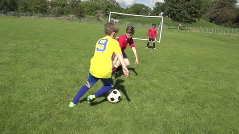 Boys / Children playing soccer / football outdoors on a sunny day. One child kicks the ball past the young goalkeepr and score a goal. Slow motion