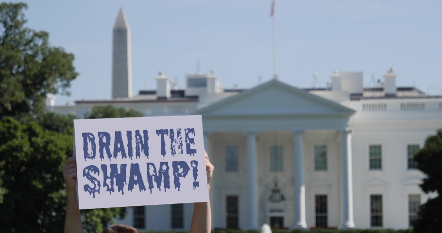 WASHINGTON, DC - Circa August, 2019 - A man holds a DRAIN THE SWAMP! election protest sign in front of the White House on a sunny summer day.  	