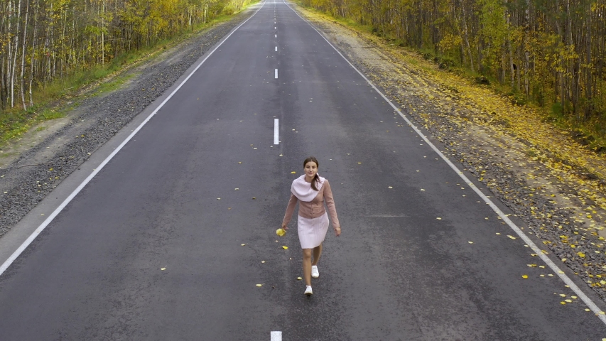 female in pink clothes runs and whirls on an asphalt road in the middle of an autumn forest. Top view.