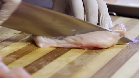 Chicken fillet on the cut board. Woman`s hands with a knife slices a delicate chicken fillet on a wooden cut board. Chicken meat on the table.