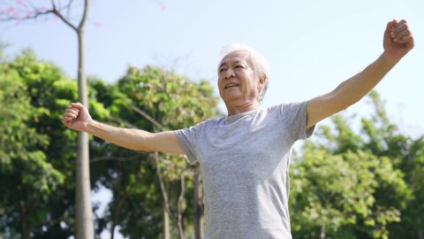 happy asian old man exercising stretching arms outdoors in park