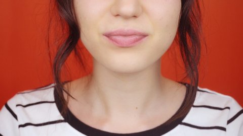 Woman with lipstick makeup eats yogurt from a spoon. A brunette woman on a bright red background is eating yogurt. Close-up of puffy lips.
