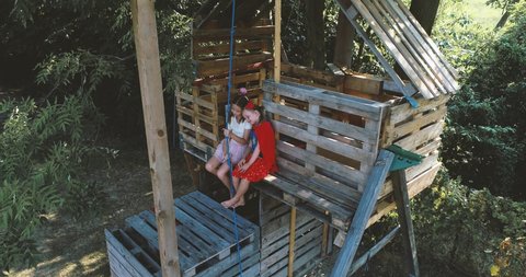 Girls wearing superhero disguises, sitting on treehouse