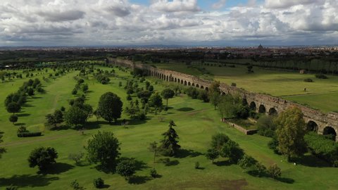 Flight over an ancient roman aqueduct next to a golf course. Rome in the background