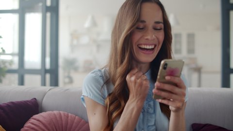 Portrait of happy business woman enjoy success on mobile phone at home office. Closeup joyful girl reading good news on phone in slow motion. Surprised lady celebrating victory on phone in apartment.