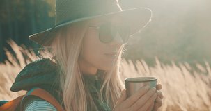 Woman hiking backpacker traveler drinking hot tea and relaxing in the fall forest on sunny autumn day. Beautiful mountain landscape view. 4K slow motion video.