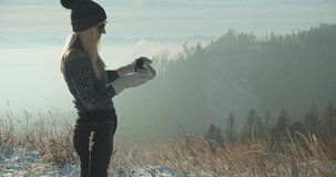 Woman traveler drinking hot tea and relaxing in the forest on sunny winter day. Beautiful mountain landscape view. 4K slow motion video.