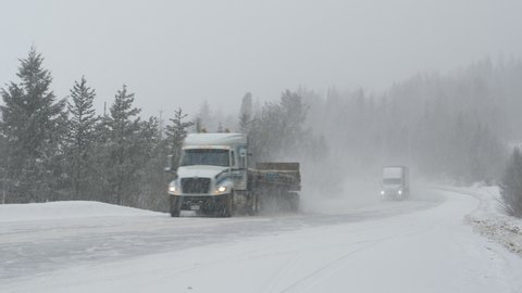 Cars and truck carefully move along a country road during a punishing snowstorm. Freight truck leads the way for other vehicles driving through a blizzard covering rural Canada with fresh snow.