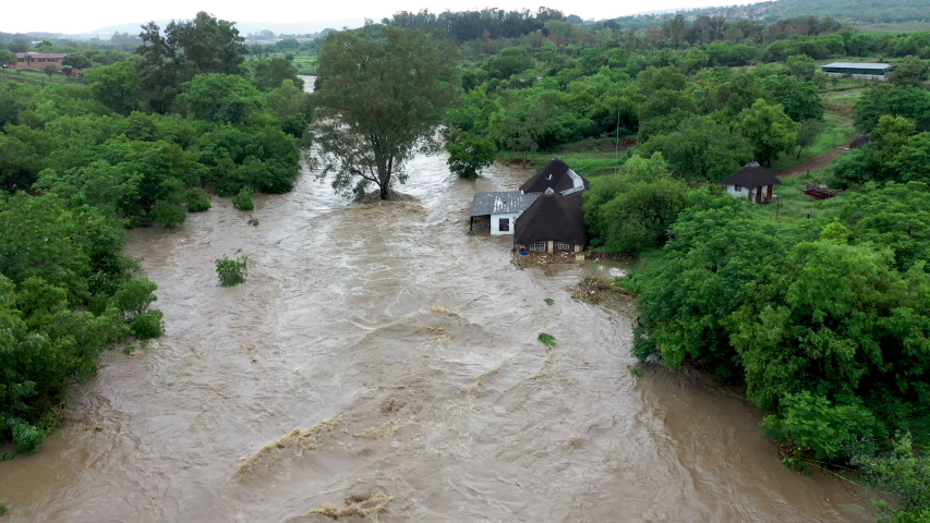 Aerial view of a river coming down in flood due to heavy rains from climate change, flooding a house on the river bank