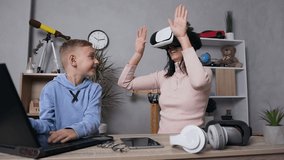 mother which using augmented reality goggles and handsome high-spirited 7-aged boy typing on computer, standing near her