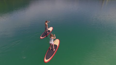 AERIAL: Girlfriend and boyfriend SUP boarding towards the lake island Bled