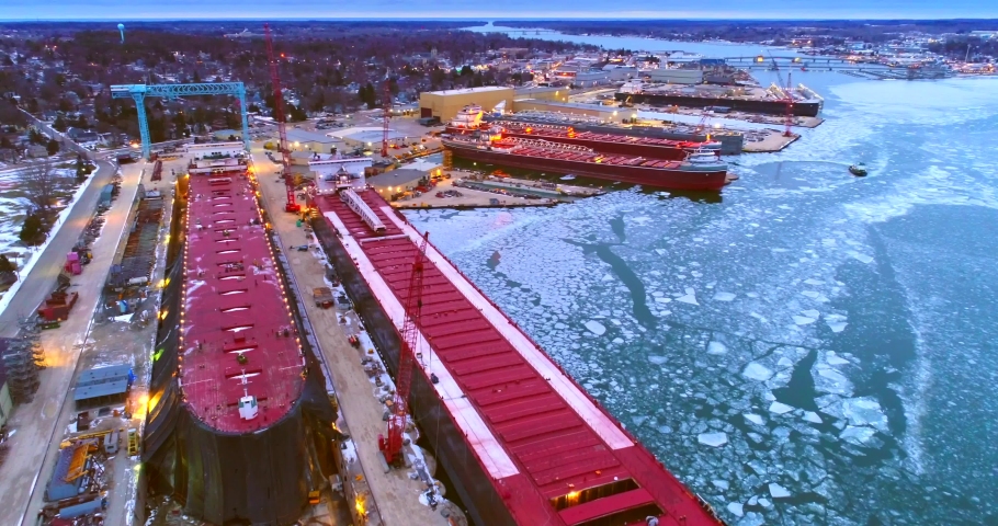 Giant Great Lakes freighter ships being built, refurbished, repaired, in icy cold waters, aerial view.