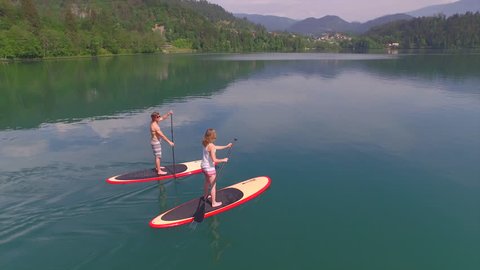 AERIAL: Young couple SUP boarding on stand up paddle board in sunny summer