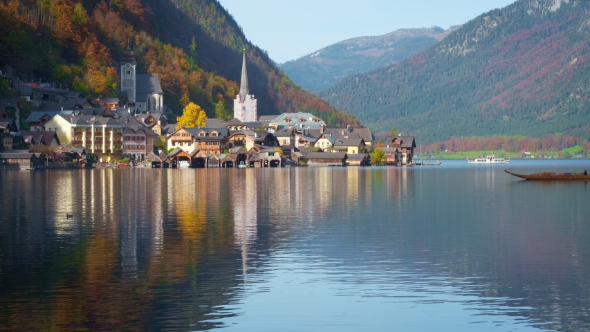 Autumn colors in famous tourist destination idillyc town Hallstatt in mountains Alps. Cathedral church, local houses, golden leaves on trees on high hills and boats floating on lake. Austria