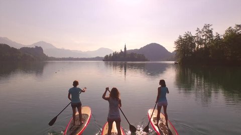AERIAL: Girls SUP paddling towards the island in the middle of the lake at sunrise