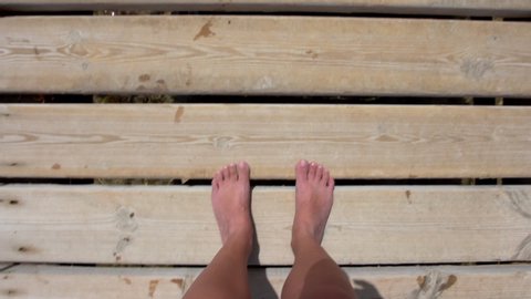 Point of view video shoot of woman walking barefoot at wooden boardwalk at sea beach. Real time full hd footage.