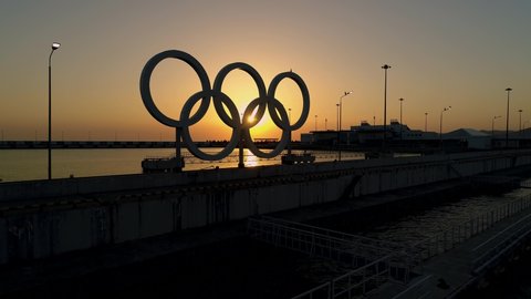 Sochi / Russia - 08.01.2019: Dark silhouette orange sunset Olympic rings on embankment of Sochi port Russia. Soviet concrete symbol sport. Sea horizon. Romantic seascape. Aerial forward
