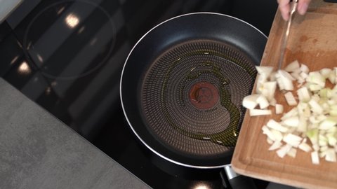 man prepares a dish at home. The girl throws onions into a frying pan from a wooden cutting board. the olive oil is soon heated to fry the onions. natural and healthy dishes. vegan food. self-isolatio