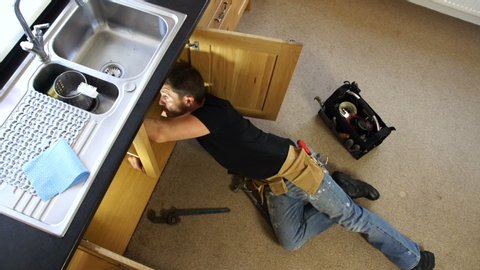 Plumber / Handyman fixing a leak. The tradesman is lying down under the sink to repair the pipe. 