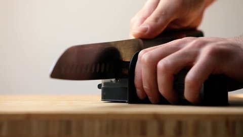 Close up of man hands sharpening knife on wooden table in kitchen