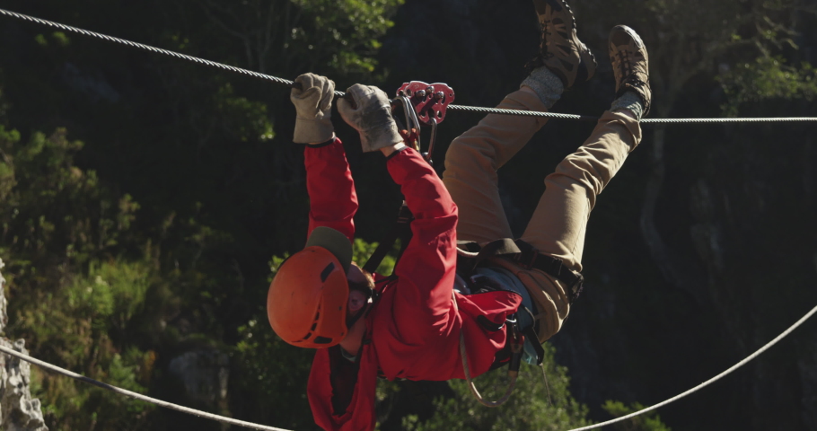 Side view of a Caucasian man zip lining on a sunny day in mountains, climbing up the rope, slow motion. Adventure Vacation in South Africa