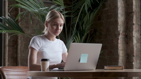 Attractive business owner woman working with laptop, drinking coffee sitting in home office. Woman working on laptop and drinking coffee at home.