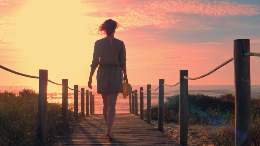 Beautiful young woman in a wooden foot bridge at the beach at sunset