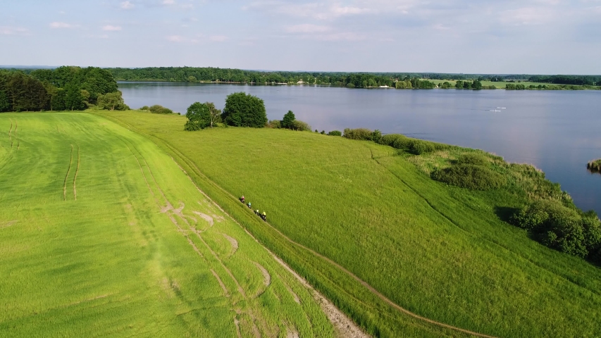 Aerial view of a group of cyclists on a green meadow by a lake