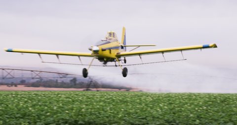 Front view of a crop duster flying low over a centre pivot irrigation system spraying chemicals over vegetable crops