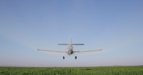Rear view of a crop duster flying low and spraying chemicals over vegetable crops