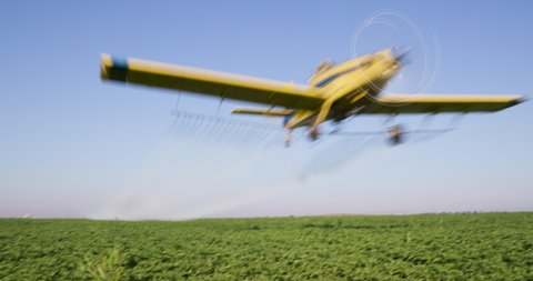 Side view of a crop duster flying low and spraying chemicals over vegetable crops
