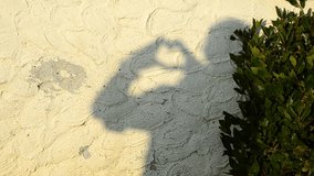 Shadow on light stucco wall. Shadow at hands of man in form of beating heart. Fun, humor and game concept. Selective focus video. Close-up.