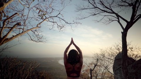 Yoga student sits in namaste pose meditating on a beautiful mountain taking in the peaceful nature setting
