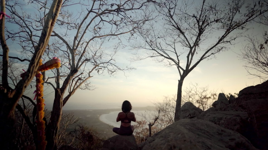 Young woman sits in namaste pose meditating on a beautiful mountain as sun sets in the distance Royalty-Free Stock Footage #1044687295