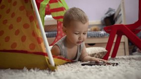 Charming baby plays with the phone in the children's tent. He watches videos and pictures. 