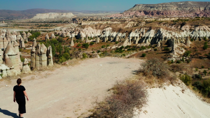 Woman walking towards the edge of a cliff in Love Valley, Cappadocia, Turkey. Aerial left to right pan with woman center frame
