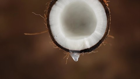 Coconut milk, dripping coconut water, drops of coco nuts oil over brown background. Tropical Coco nut closeup. Healthy Food, skin care concept. Vegan food. 4K UHD video, slow motion