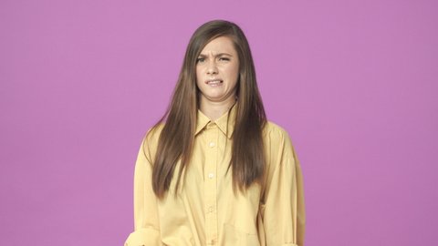 Slow-motion attractive stylish young 20s woman cringe from aversion, squinting, wrinkle nose, grimacing as if looking at something disgusting, very ugly and unpleasant, dislike it, purple background