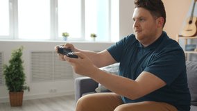 Happy young man is playing video game at home winning kissing joystick having fun alone in modern apartment. Technology, youth and happiness concept.