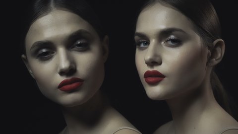 Faces of girls in the dark. Faces of two twin sisters on a dark background. Red lipstick. Perfect skin. Nude makeup.