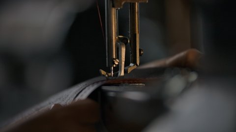 Close-up view of working sewing machine presser foot, stitching in slowmotion. Tailor's hand holding sewing leather carefully. Manufacturing handicraft unique individual bags, belts, accessories 