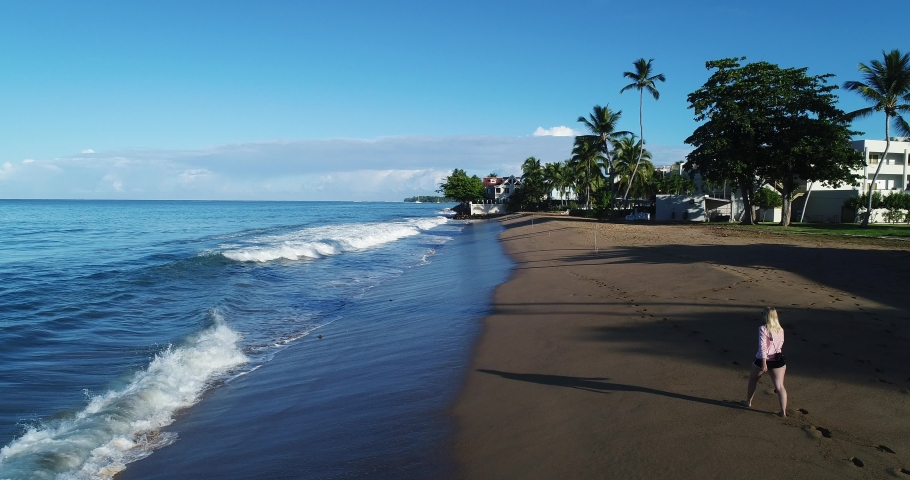 A young female traveler walks along the beach on a beautiful sunny afternoon in Rincon, Puerto Rico, as the waves wash up on the sand.