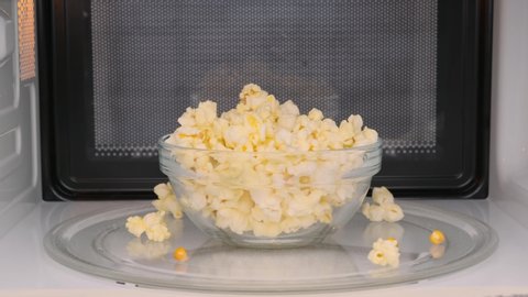 Woman takes out cooked popcorn in transparent bowl from microwave oven close-up.