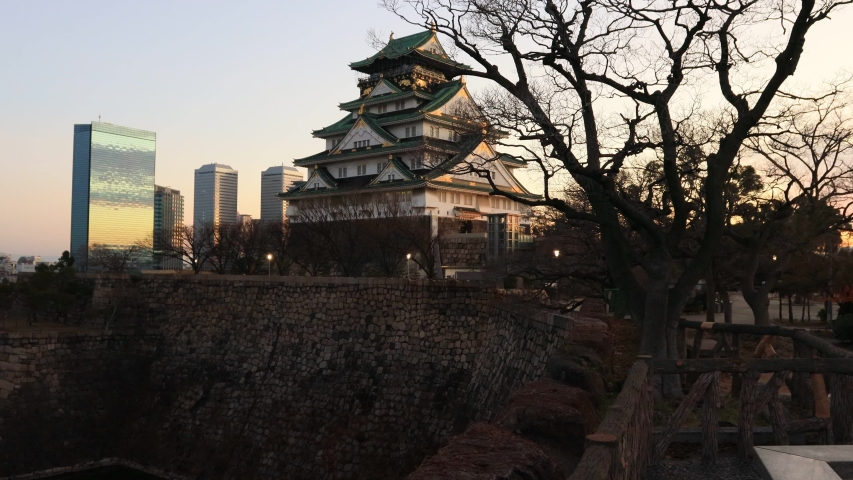 The main keep and multi-layered white tower of Osaka castle above stone walls and water moat at sunrise.
