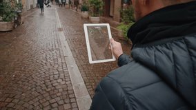 Close up of an young man is making a video call to his girlfriend with a futuristic latest innovative technology glass tablet with augmented reality holograms during walking in city center by day.