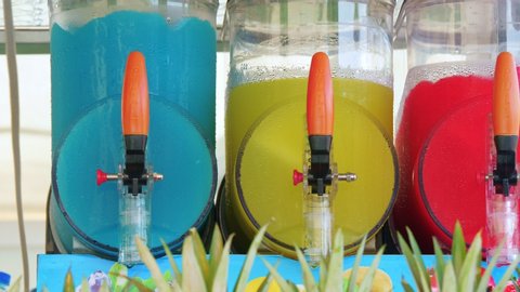 Freezing and mixing machines for making ice slushy drinks containing blue, yellow and red slush. Cold colorful frozen sugar juice.