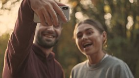 Close up view of Joyful young pretty couple making selfie on smartphone in park outdoors