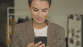 A beautiful young businesswoman is using a smartphone then looking to the camera indoors