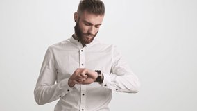A handsome serious bearded man is using his smart watch or fitness tracker isolated over white wall background